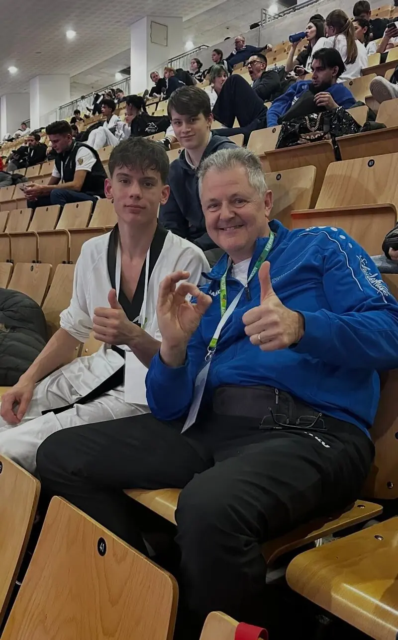 Ein Sportler im Dobok und sein Trainer auf der Tribüne, beide zeigen den Daumen nach oben