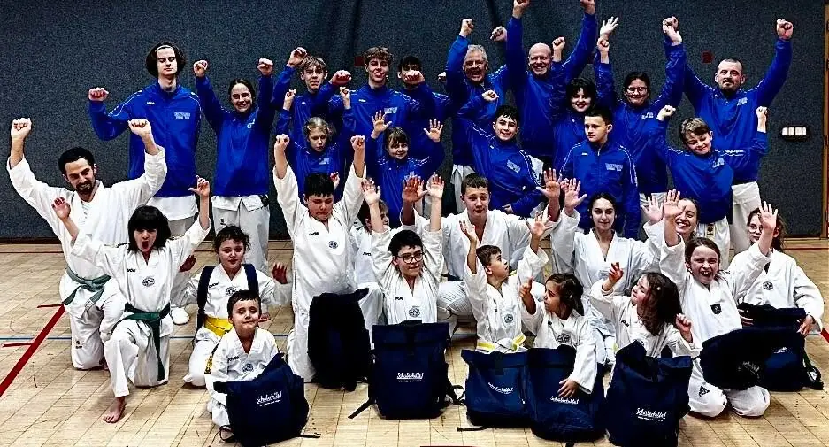 Jubelndes Gruppenfoto zum Jahresabschluss 2025: vorne Kinder und Erwachsene im Dobok, dahinter Sportlerinnen, Sportler und Trainer in blauen Vereinsjacken