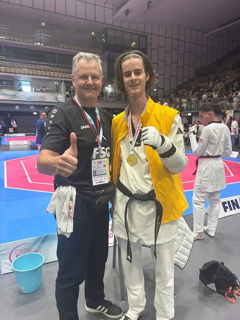 Ein Sportler im Dobok mit Goldmedaille und sein Trainer an der Wettkampffläche bei der ÖM 2025