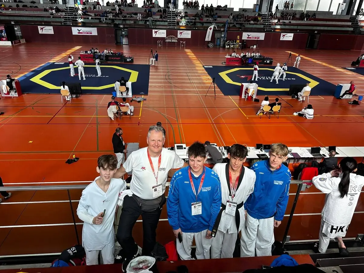 Vier Sportler unseres Teams mit ihrem Trainer auf der Tribüne über den Wettkampfflächen der Swiss Open 2025 im Athletikzentrum St. Gallen
