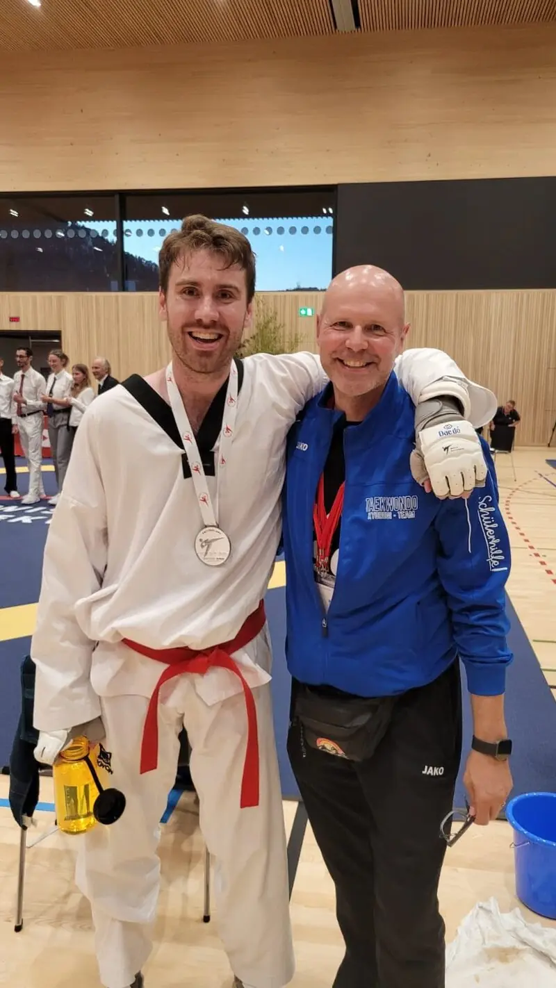 Ein Sportler unseres Teams im Dobok mit Medaille, Arm in Arm mit seinem Coach, bei der Wattwil Open 2025