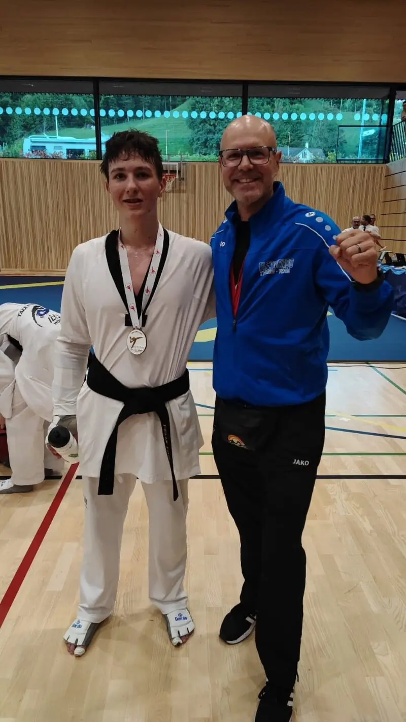 Ein junger Sportler im Dobok mit Medaille neben seinem jubelnden Coach bei der Wattwil Open 2025